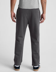 man wearing a gray shirt and gray straight leg sweatpants on a plain background.
