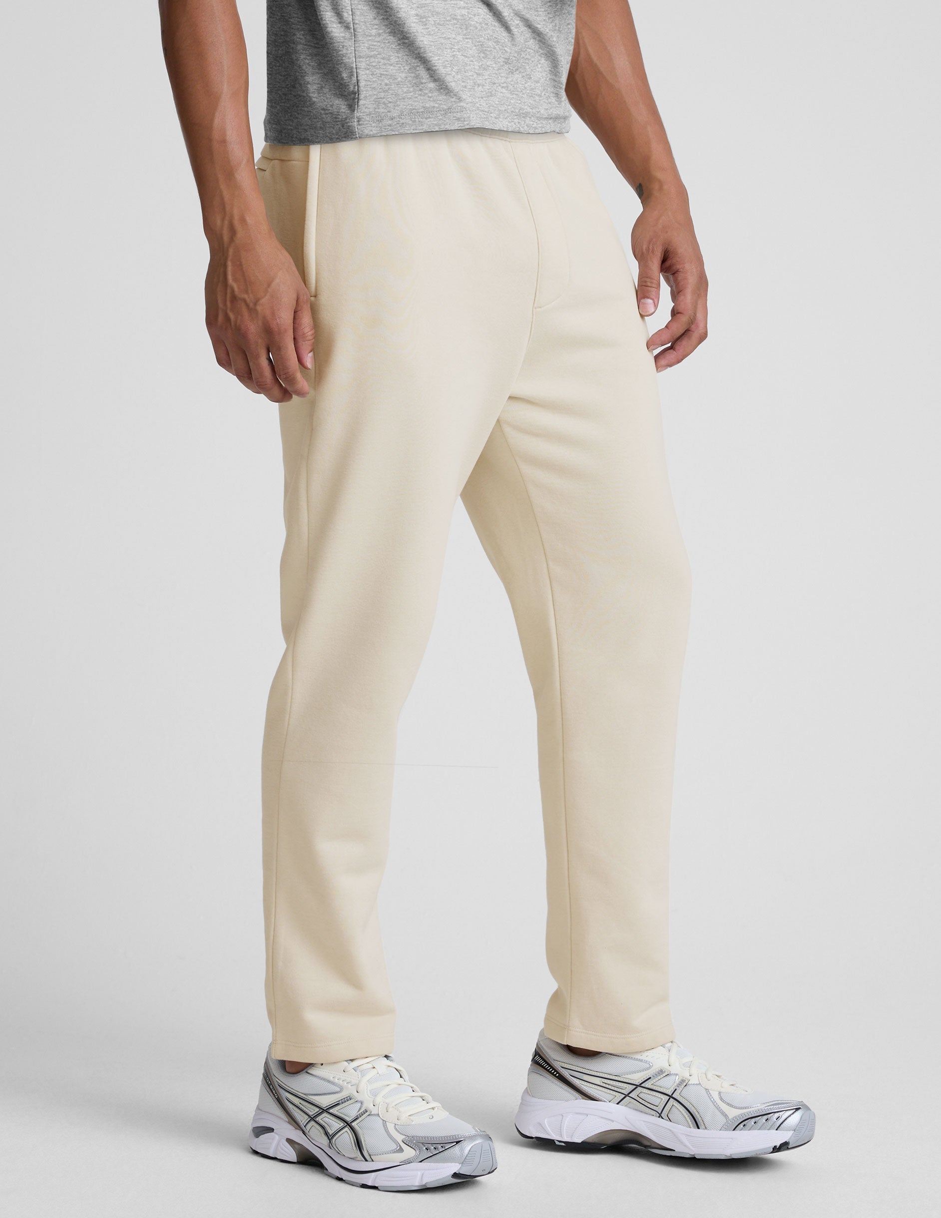 man wearing a cream-colored straight leg fleece sweatpants on a plain background.