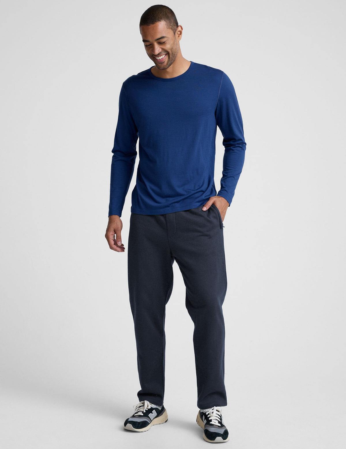 man wearing a blue long-sleeve shirt and navy blue straight leg fleece sweatpants on a plain background.