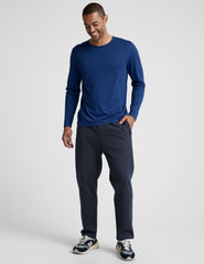 man wearing a blue long-sleeve shirt and navy blue straight leg fleece sweatpants on a plain background.