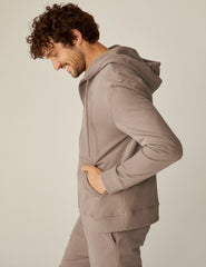 model is wearing a brown men's zip-up hooded jacket.