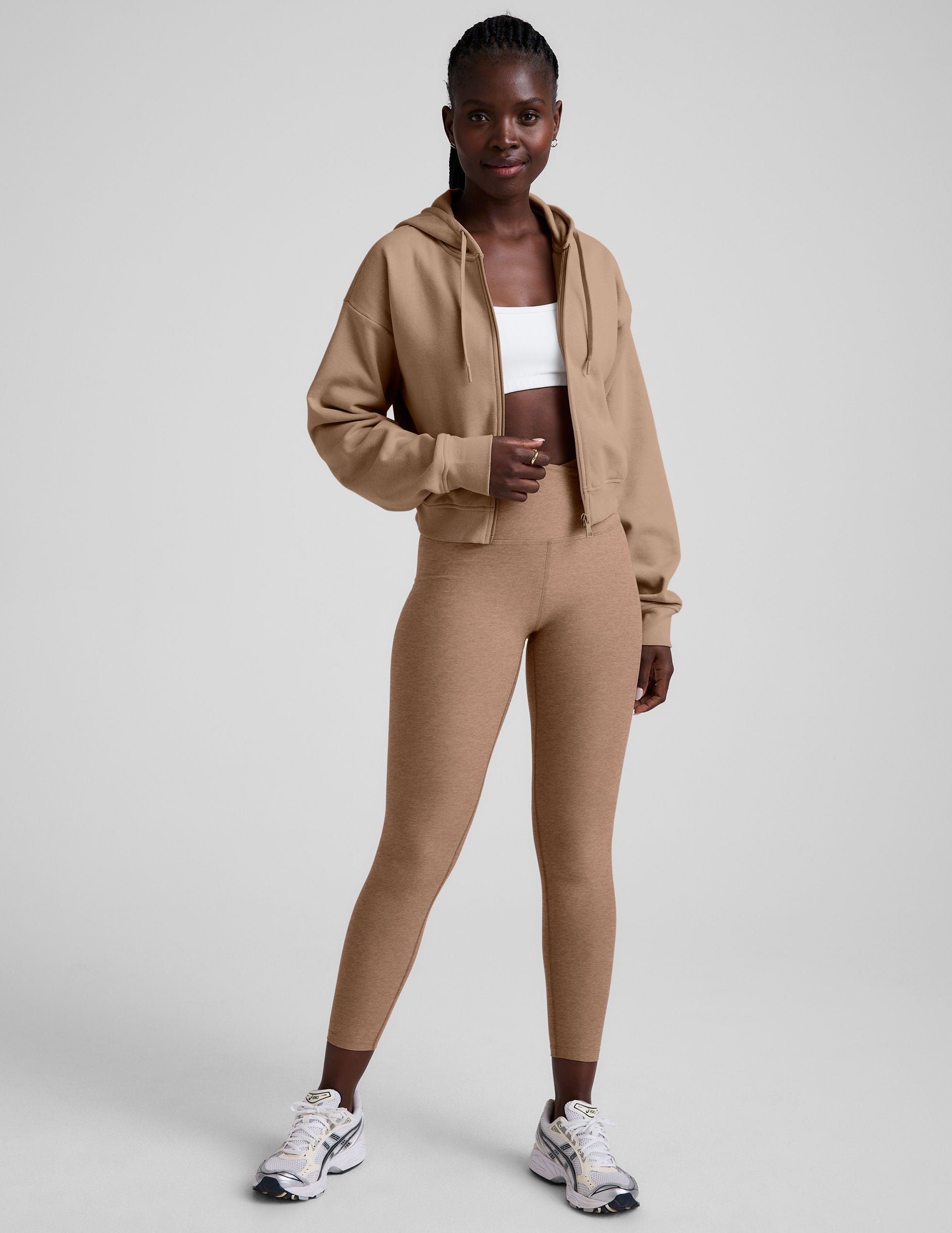 model wearing a brown fleece zip-up hoodie and leggings set on a plain background.