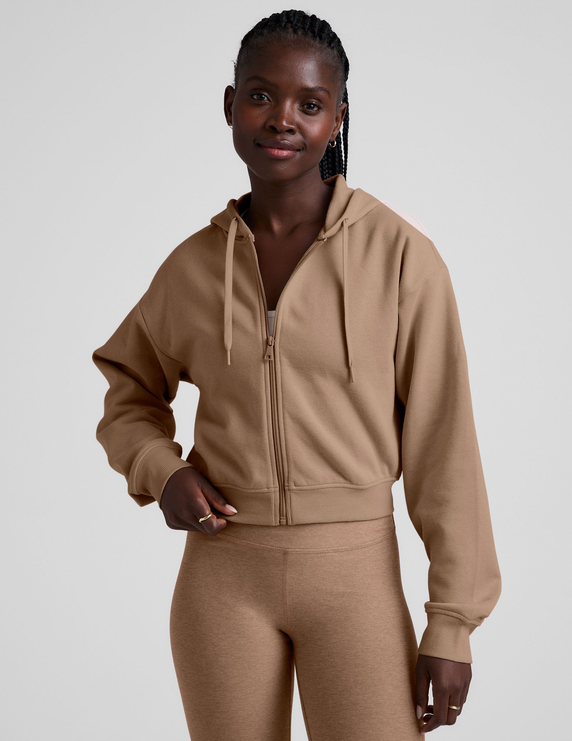 model wearing a brown fleece zip-up hoodie and leggings set on a plain background.