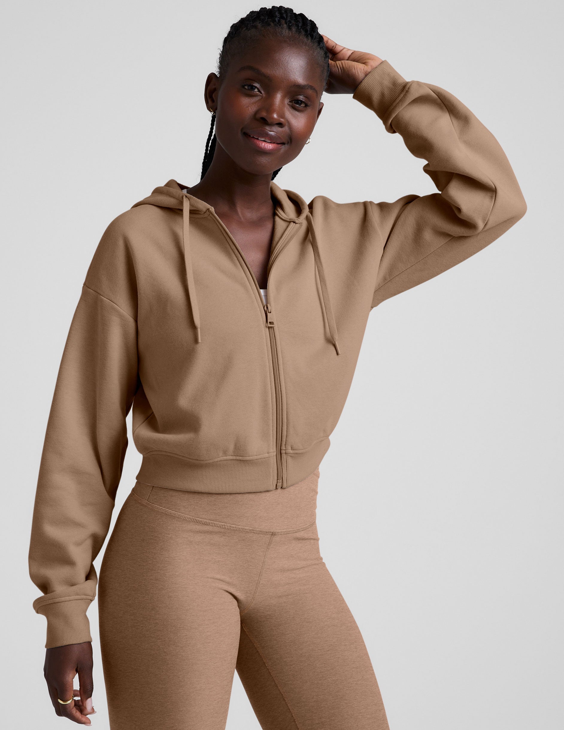 model wearing a brown fleece zip-up hoodie and leggings set on a plain background.