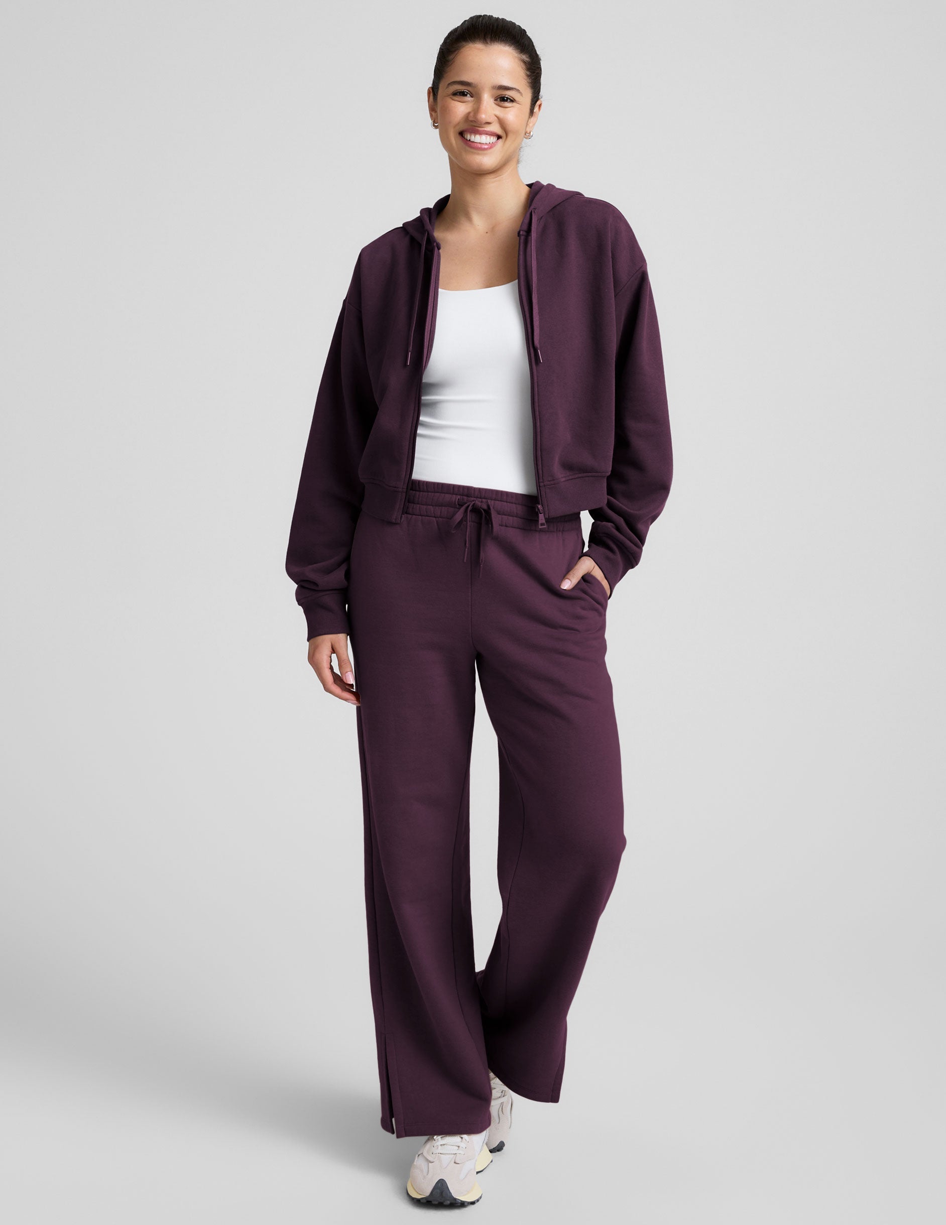 model wearing a purple fleece zip-up hoodie and fleece wide leg pants on a plain background.