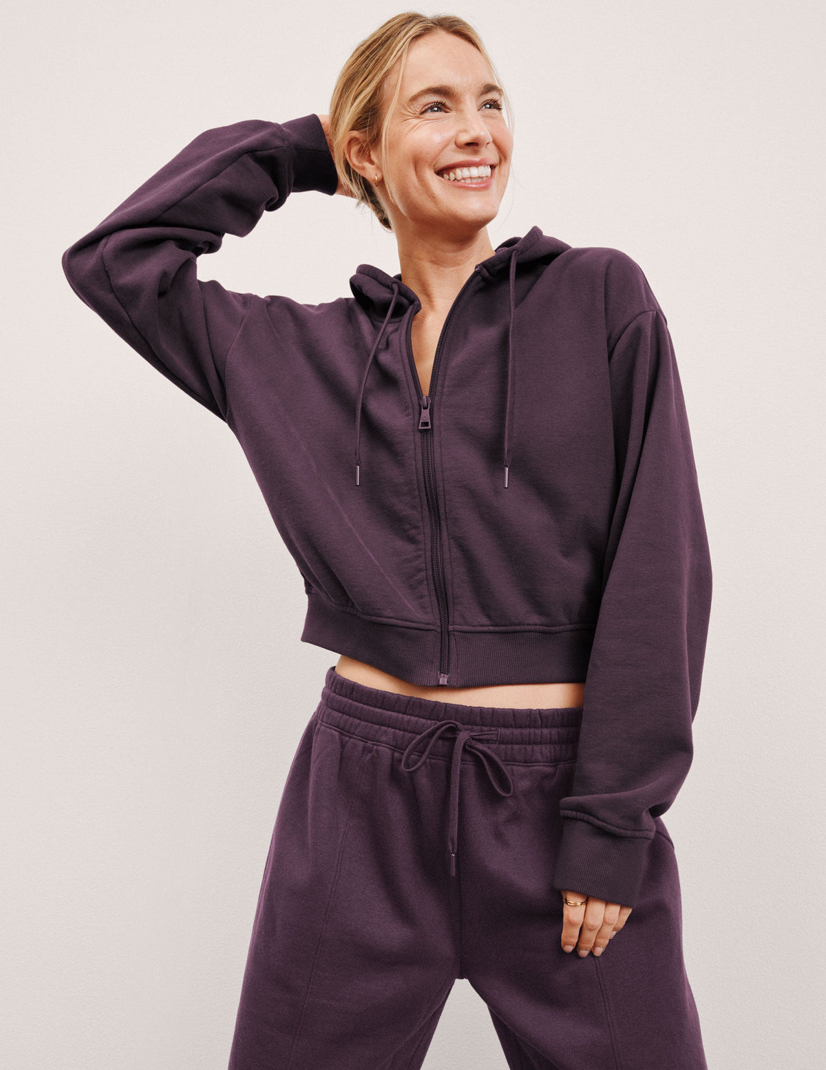 model wearing a purple fleece zip-up hoodie and fleece wide leg pants on a plain background.