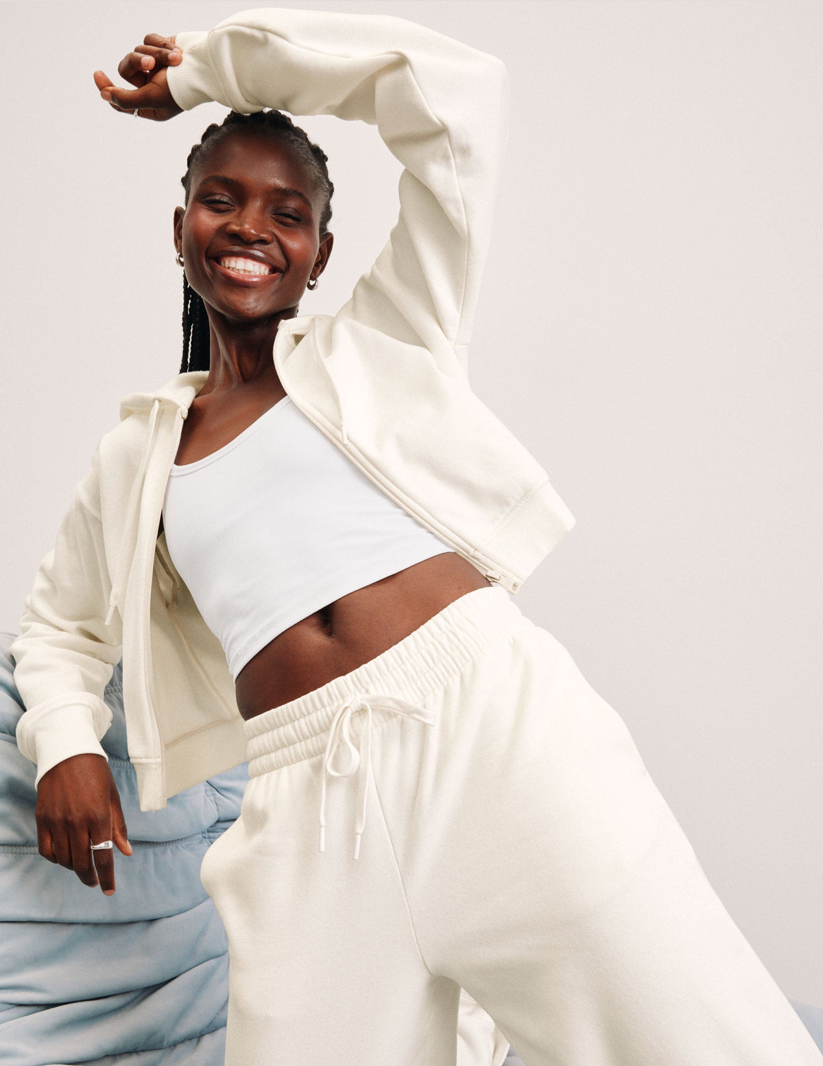 woman wearing a white zip-up jacket and white fleece pants against a plain background.