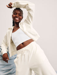 woman wearing a white zip-up jacket and white fleece pants against a plain background.