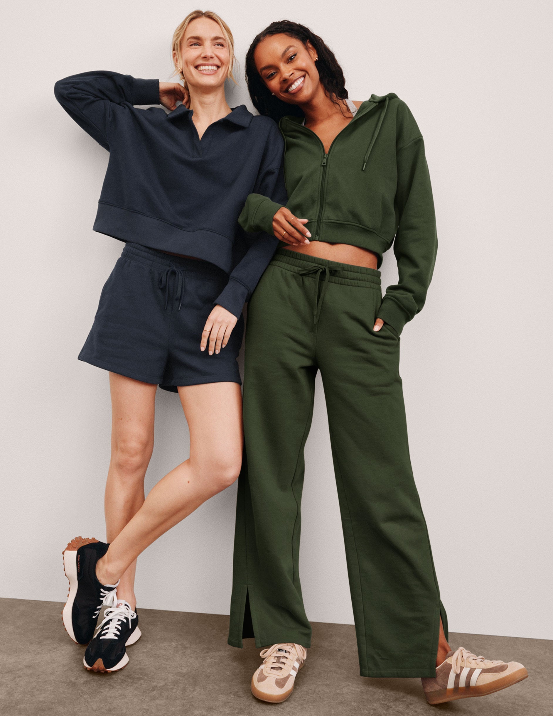 two models posing together wearing  blue and green sweat suits against a plain background.