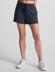 model wearing blue sweat shorts and white sneakers on a light gray background.