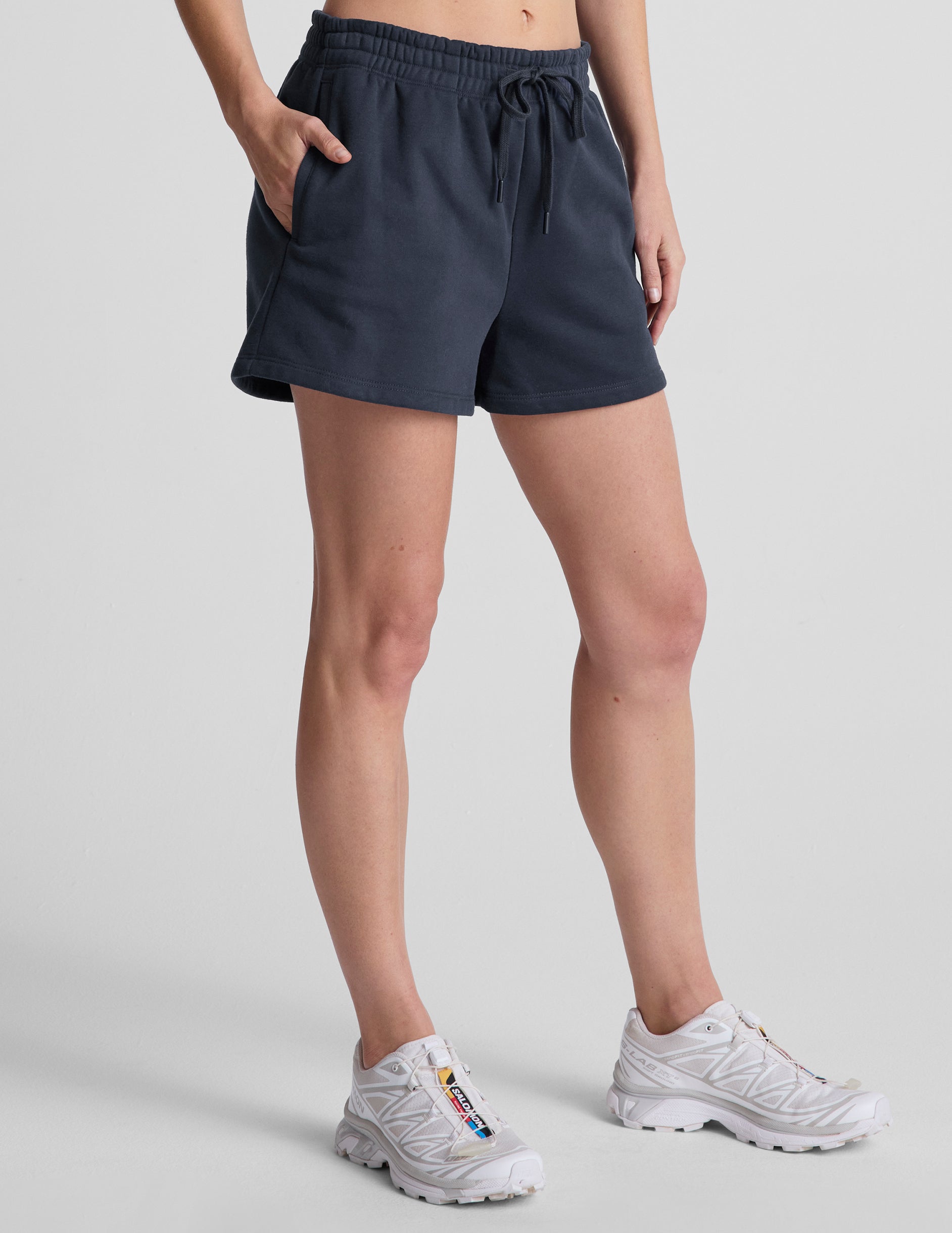 model wearing blue sweat shorts and white sneakers on a light gray background.