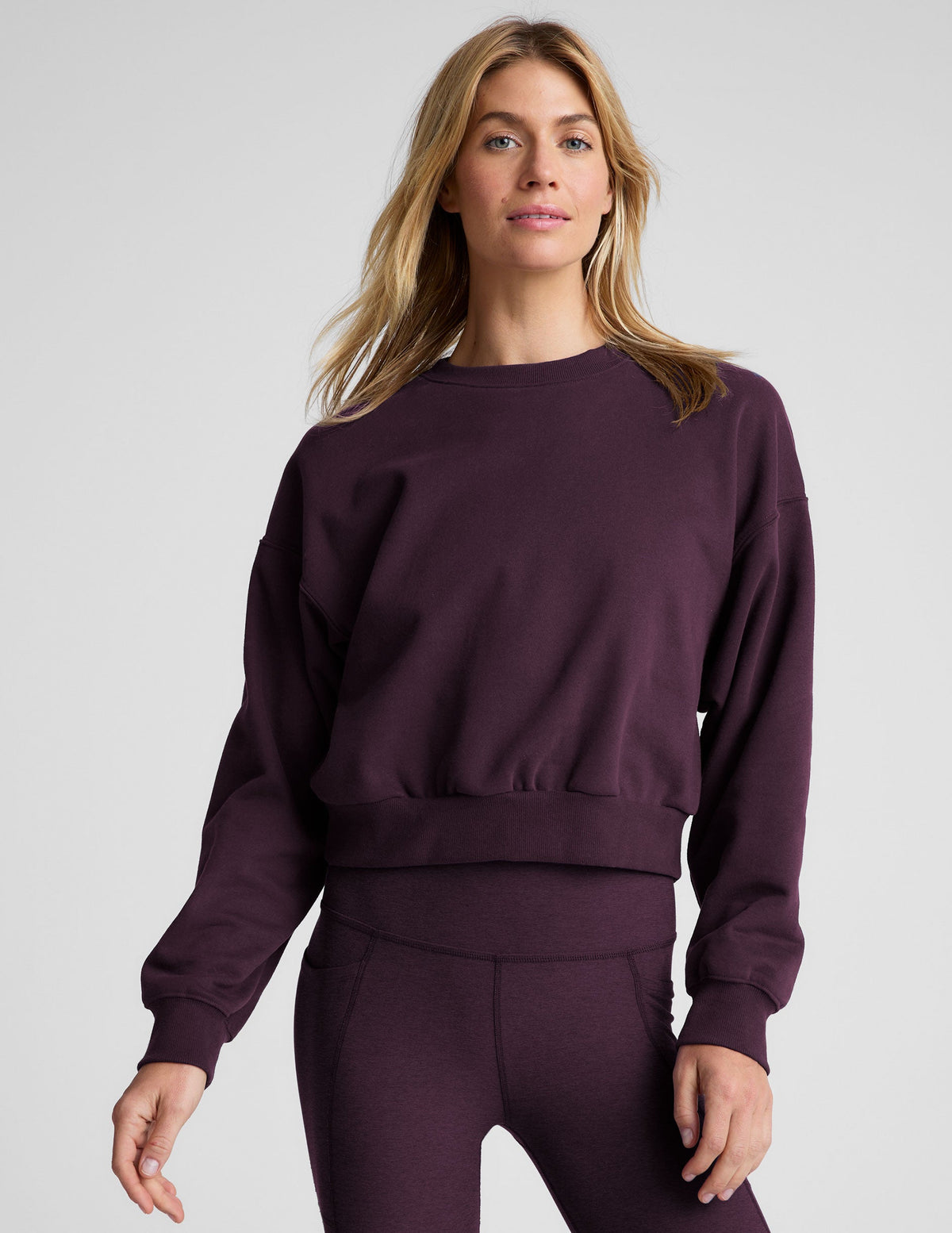 model wearing a purple fleece cropped crew neck sweatshirt and leggings on a light gray background.