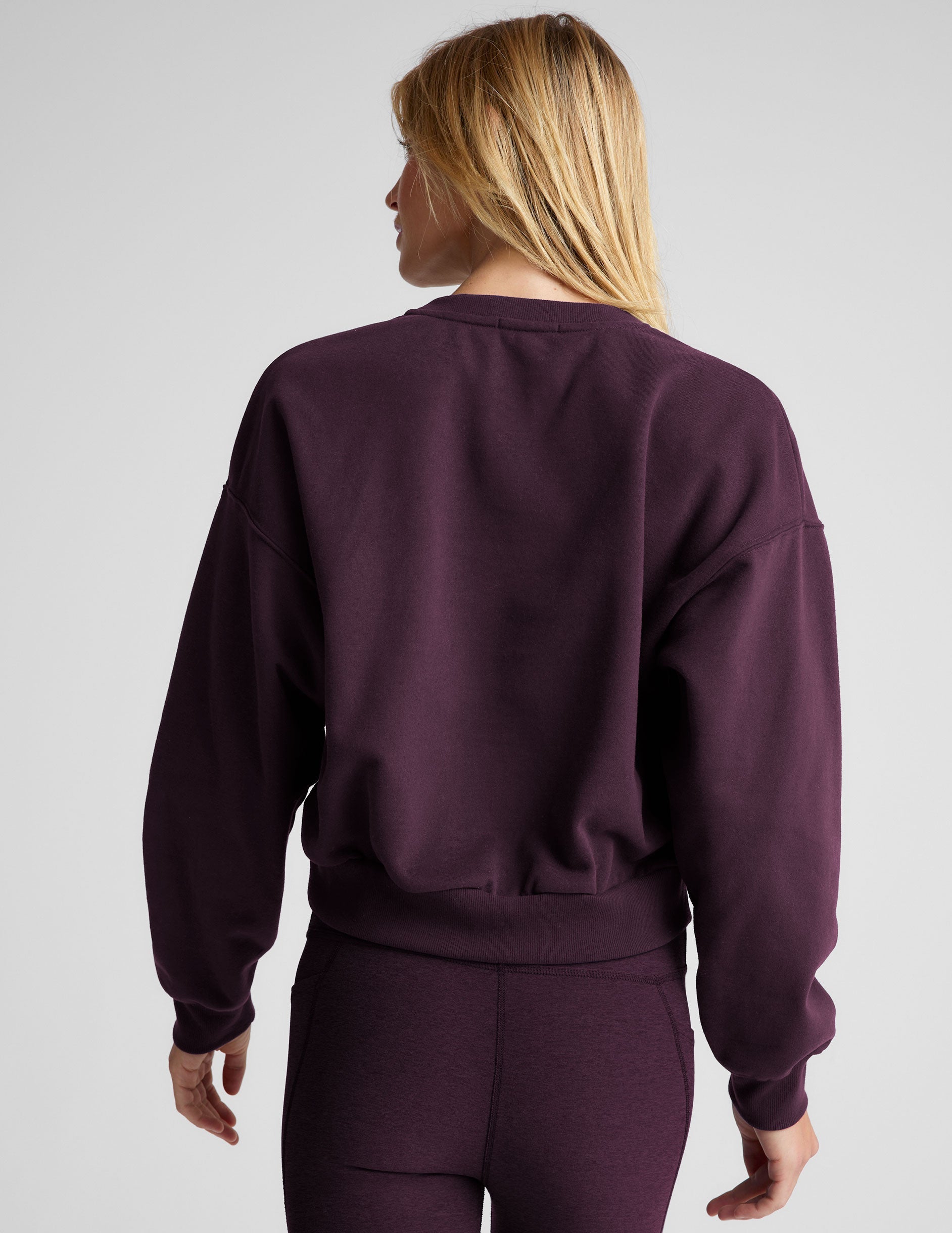 model wearing a purple fleece cropped crew neck sweatshirt and leggings on a light gray background.