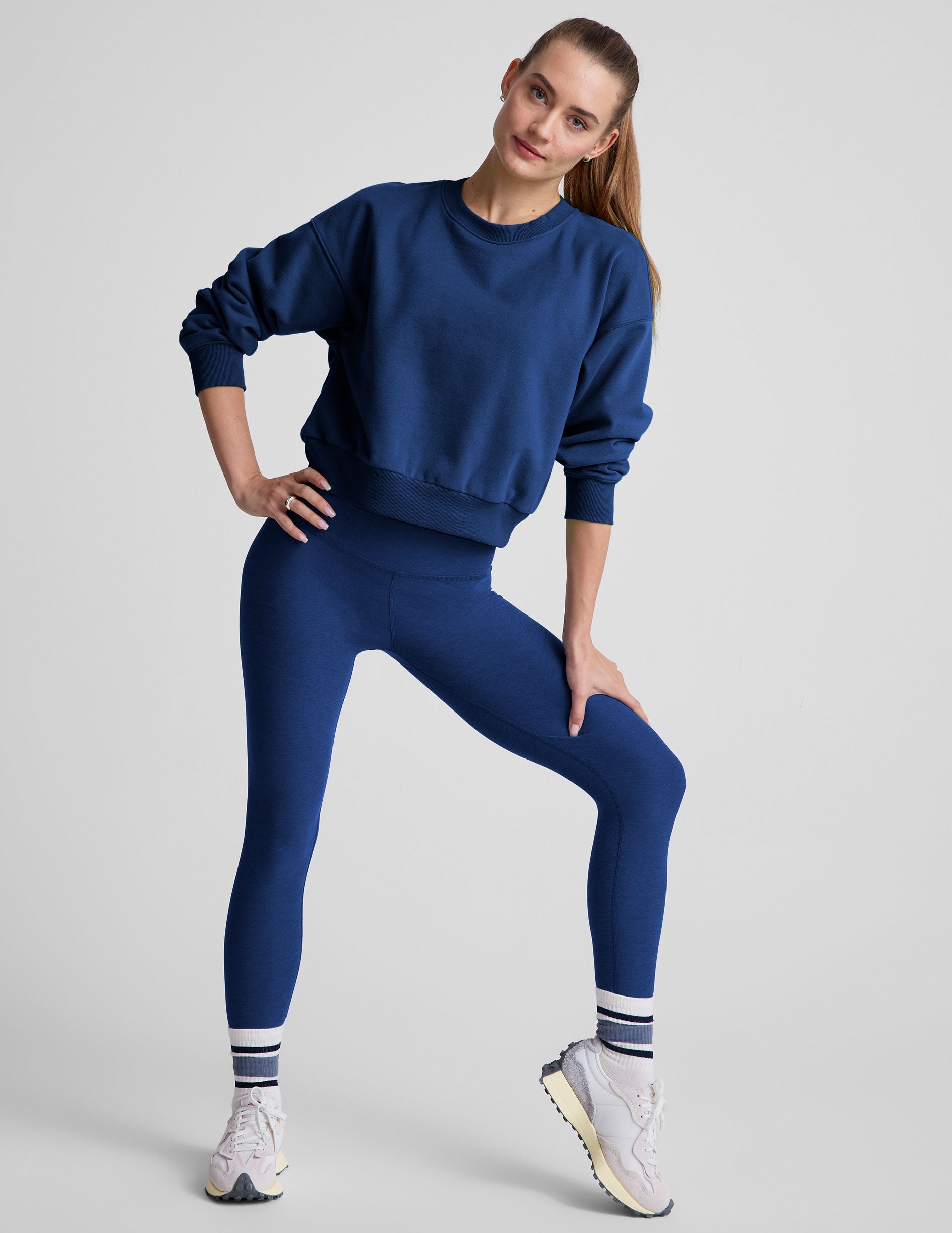 model wearing a blue crewneck fleece cropped sweatshirt and leggings against a plain background.