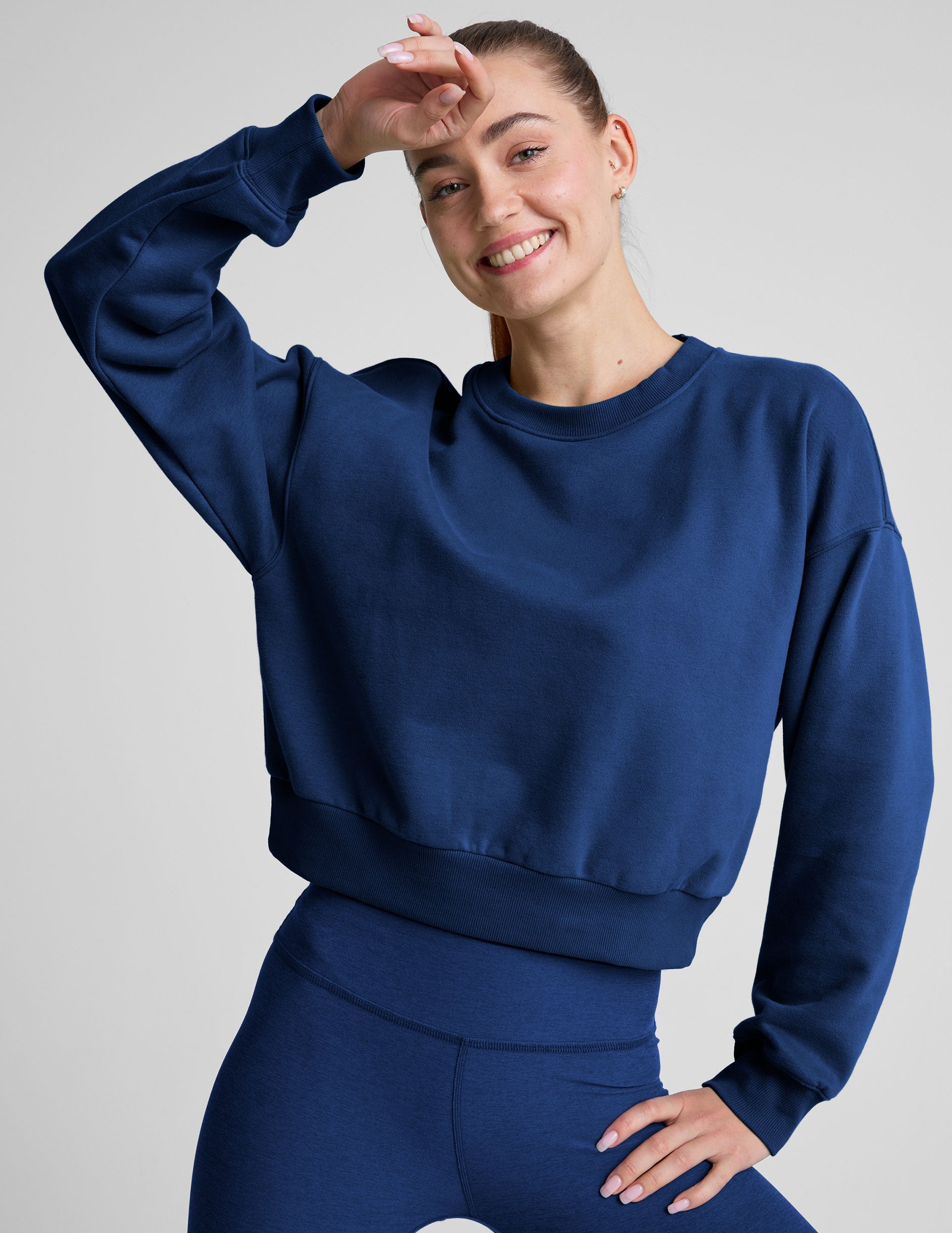 model wearing a blue crewneck fleece cropped sweatshirt and leggings against a plain background.