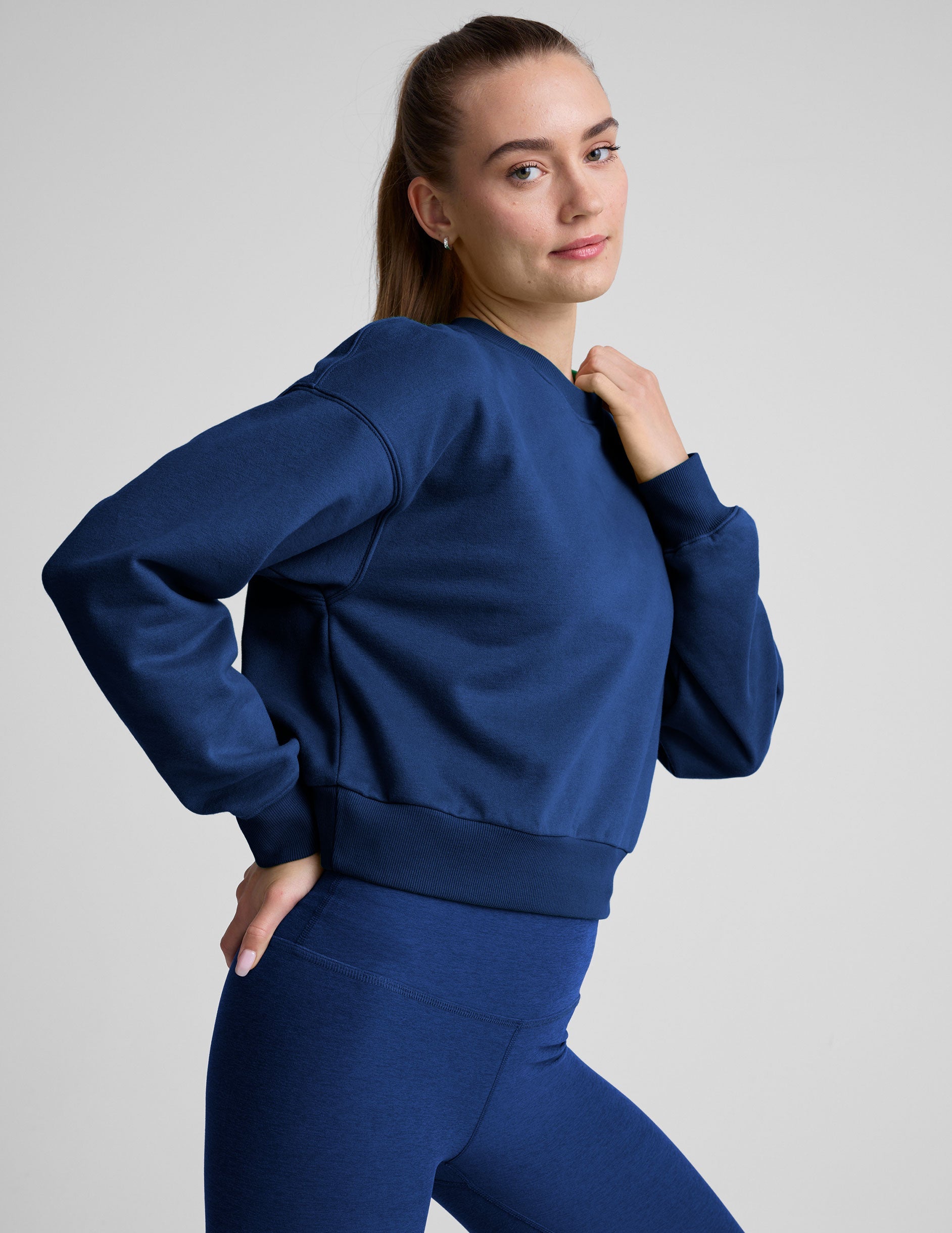 model wearing a blue crewneck fleece cropped sweatshirt and leggings against a plain background.