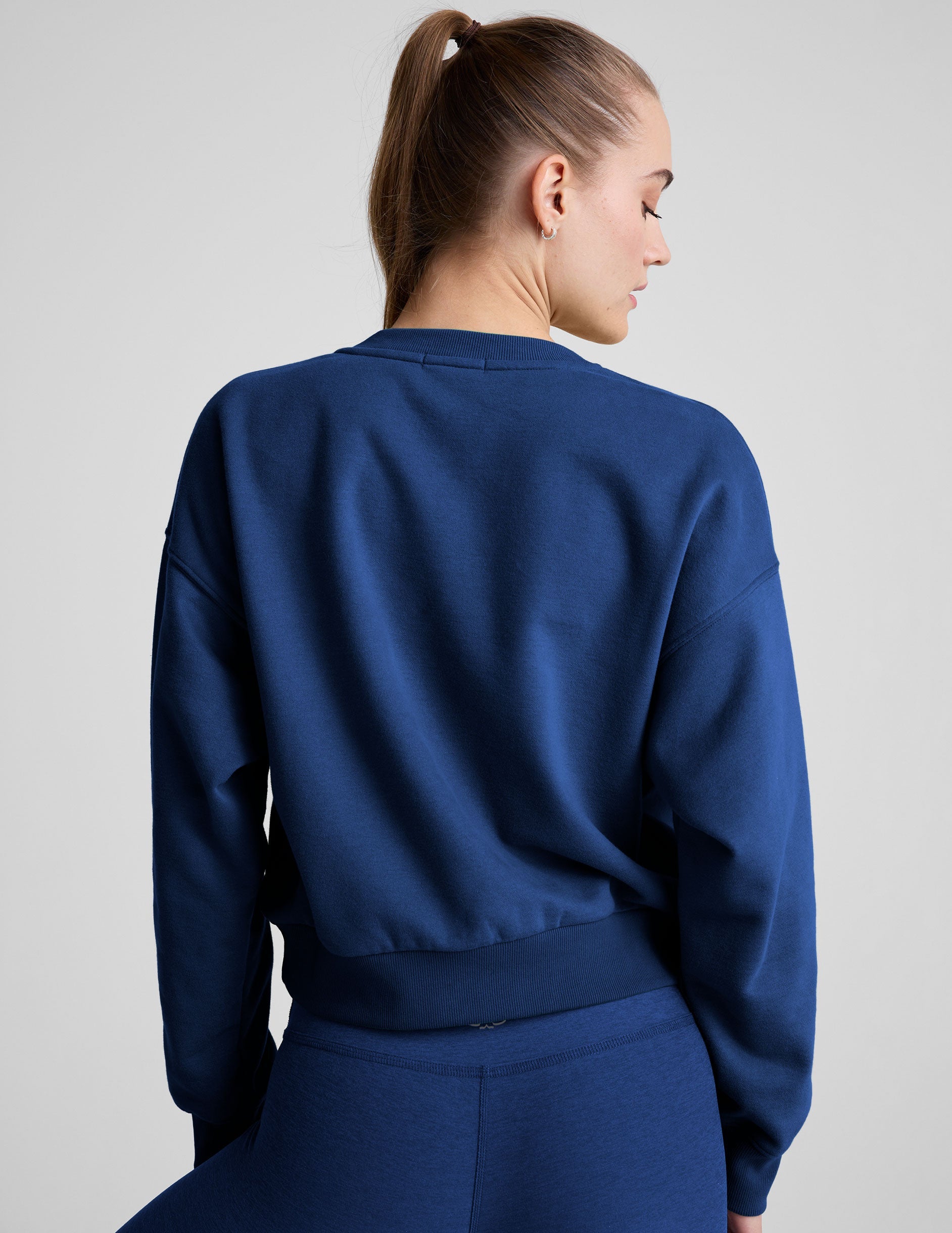 model wearing a blue crewneck fleece cropped sweatshirt and leggings against a plain background.