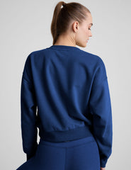 model wearing a blue crewneck fleece cropped sweatshirt and leggings against a plain background.