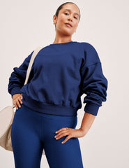 woman wearing a blue sweatshirt and leggings with a beige bag on a plain background.