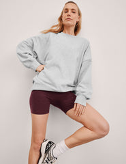 model wearing a light gray sweatshirt and maroon shorts on a plain background.