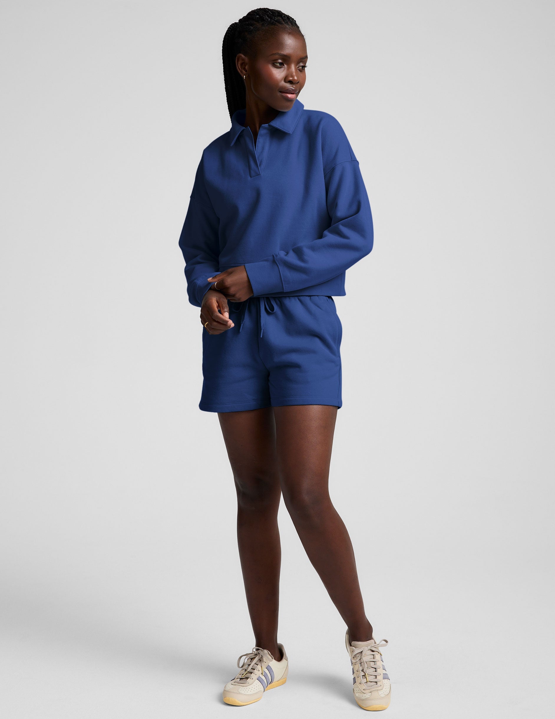 model wearing a blue cropped collared sweatshirt and blue sweat shorts on a plain background.