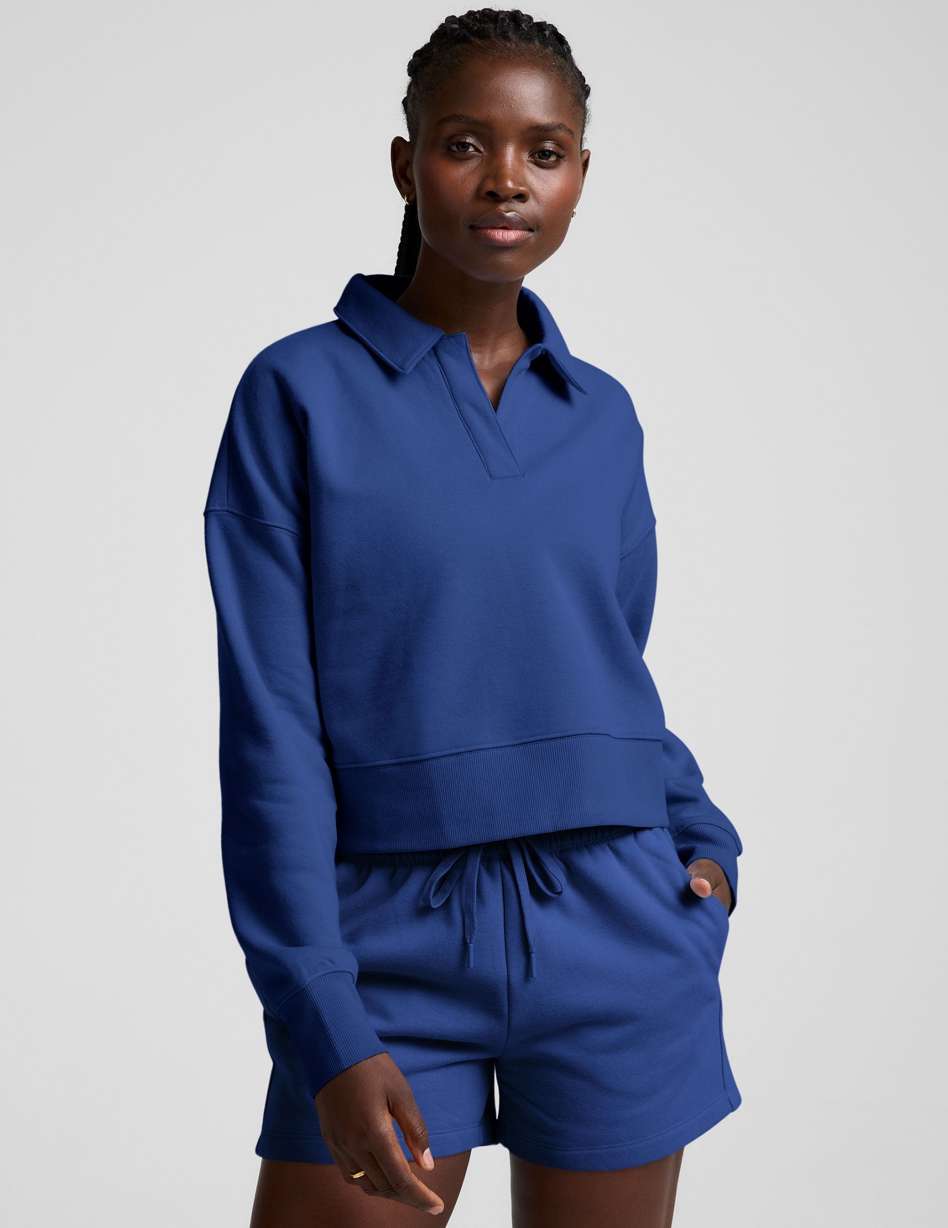 model wearing a blue cropped collared sweatshirt and blue sweat shorts on a plain background.