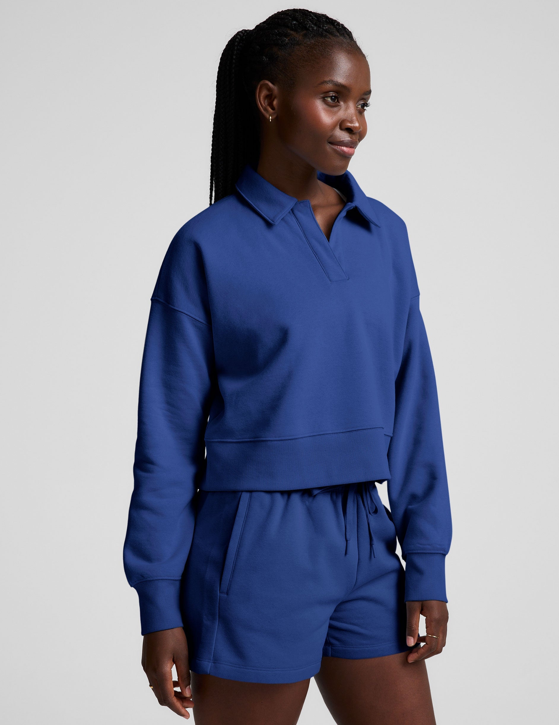 model wearing a blue cropped collared sweatshirt and blue sweat shorts on a plain background.