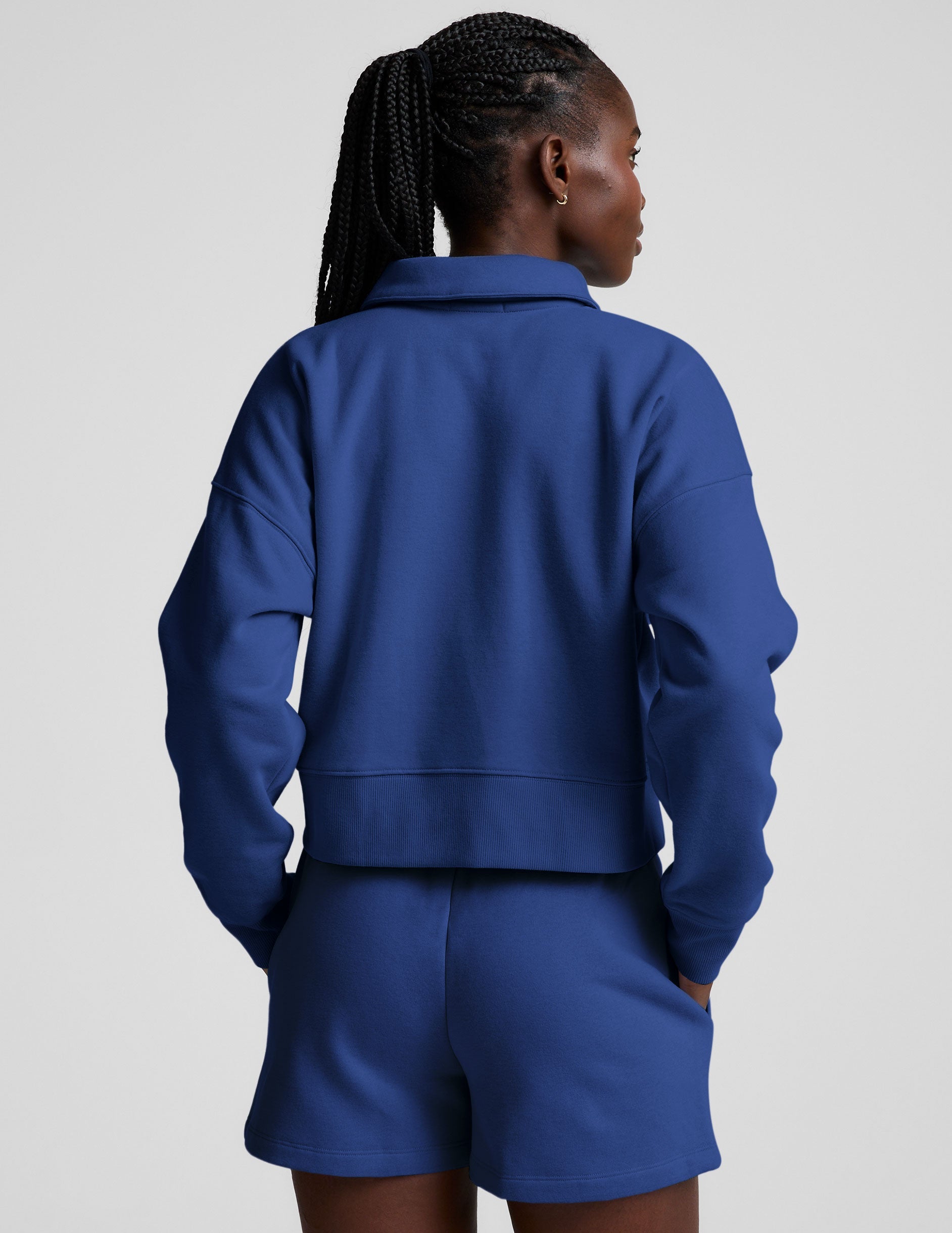 model wearing a blue cropped collared sweatshirt and blue sweat shorts on a plain background.