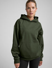 woman wearing a green oversized hoodie and black leggings on a gray background.