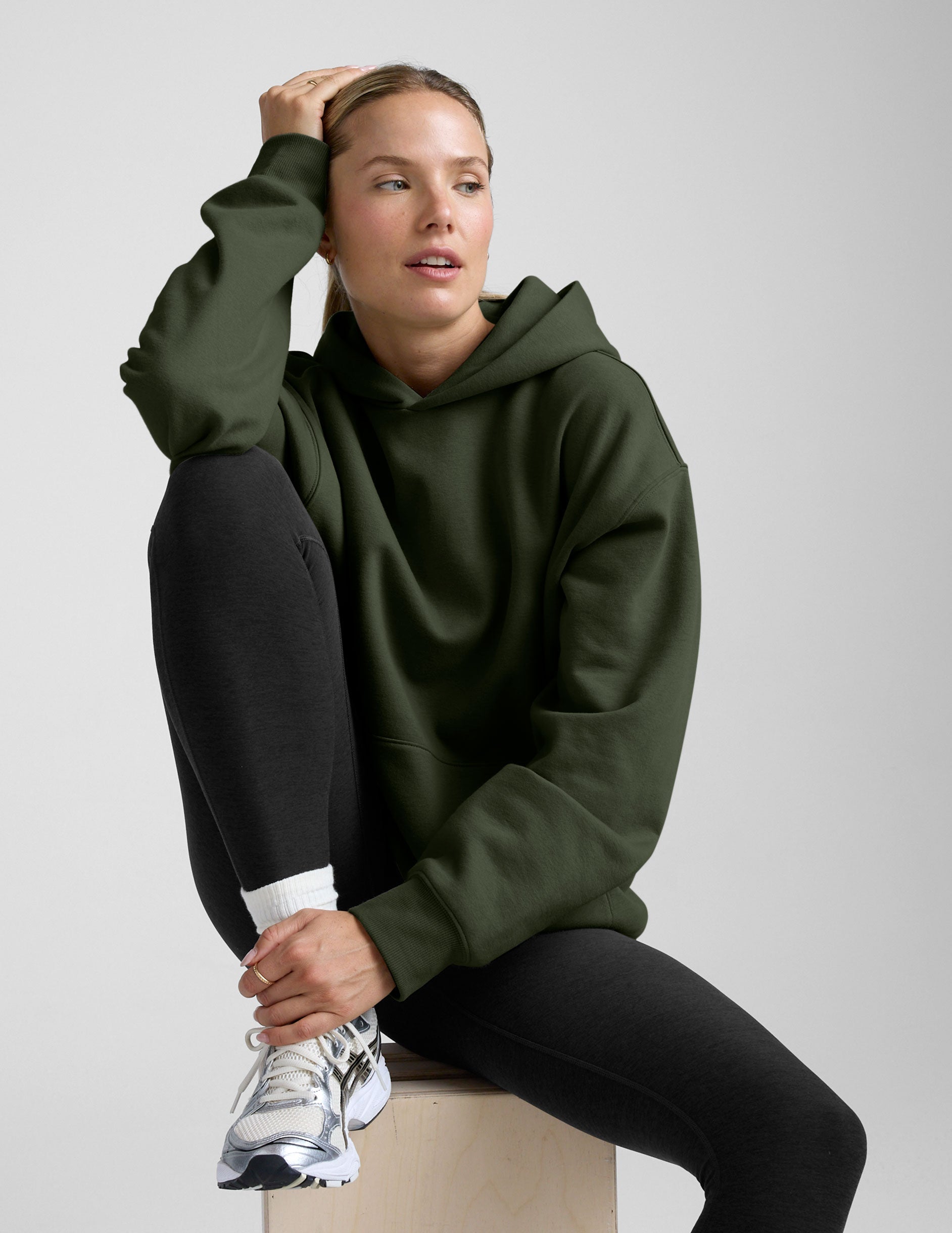 woman wearing a green oversized hoodie and black leggings on a gray background.