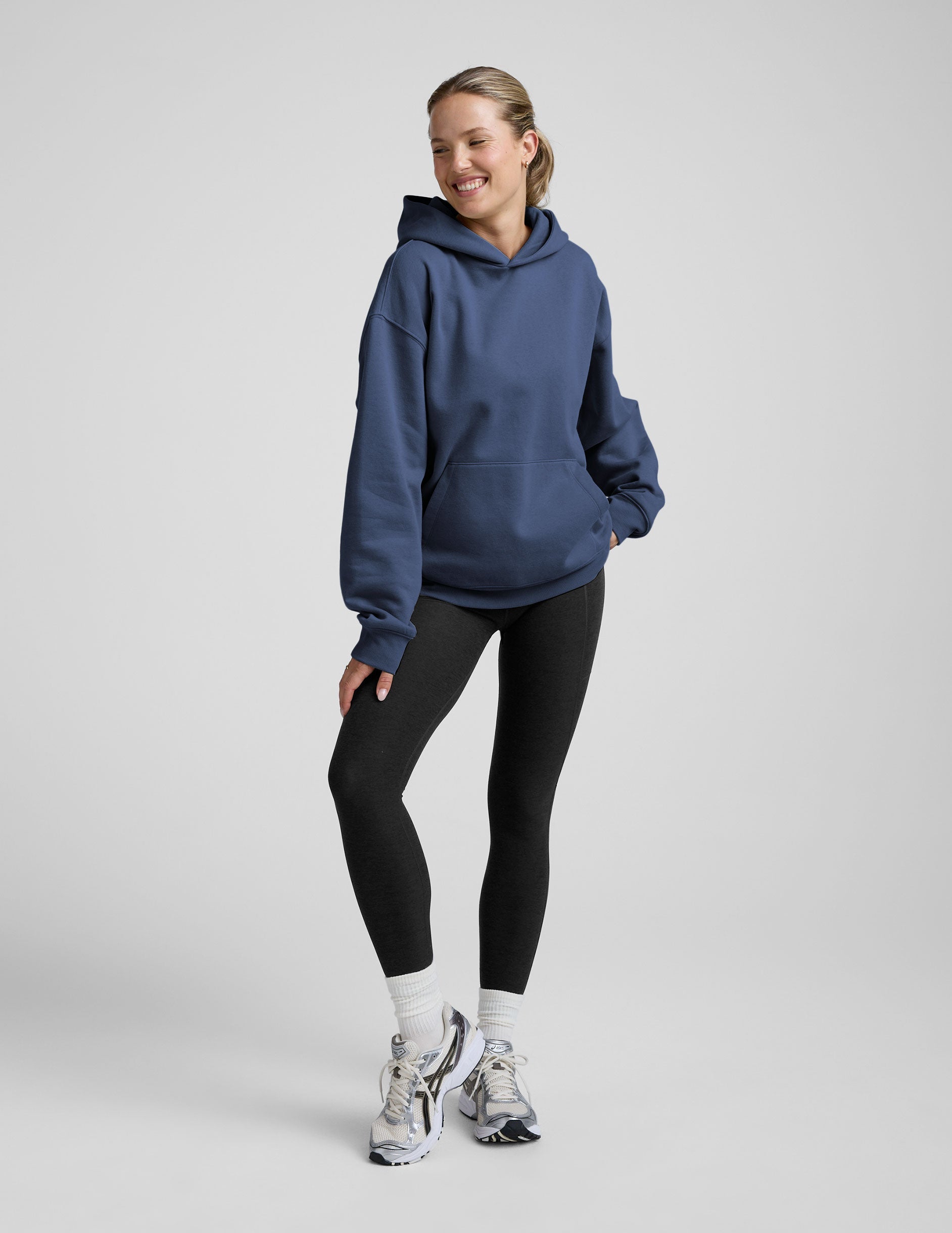 woman wearing a blue hoodie and black sweats against a plain background.