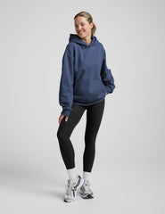 woman wearing a blue hoodie and black sweats against a plain background.