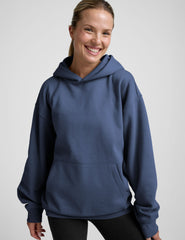 woman wearing a blue hoodie and black sweats against a plain background.
