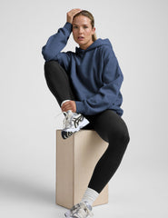 woman wearing a blue hoodie and black sweats against a plain background.