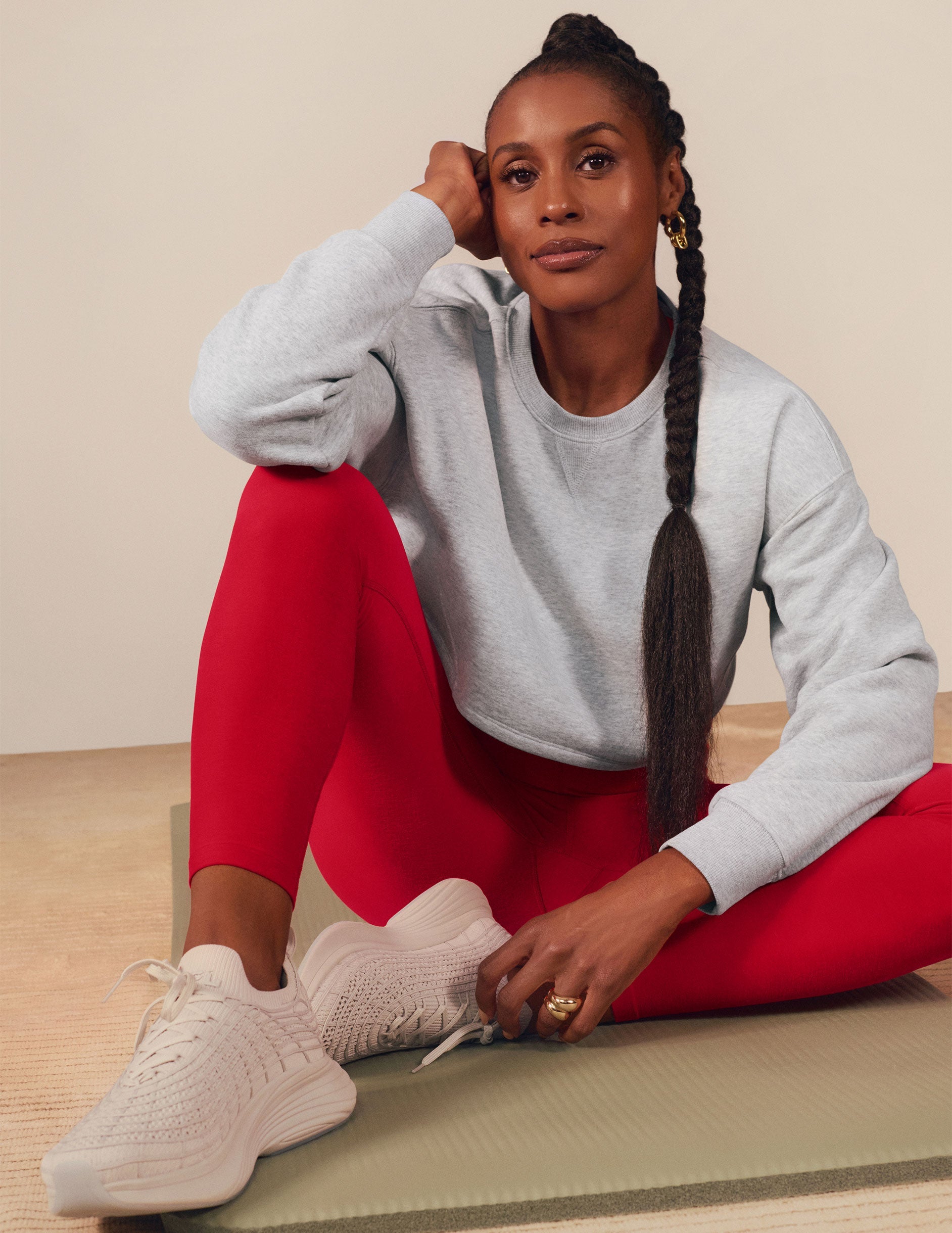 Issa Rae wearing a gray cropped sweatshirt and red pants against a beige background.