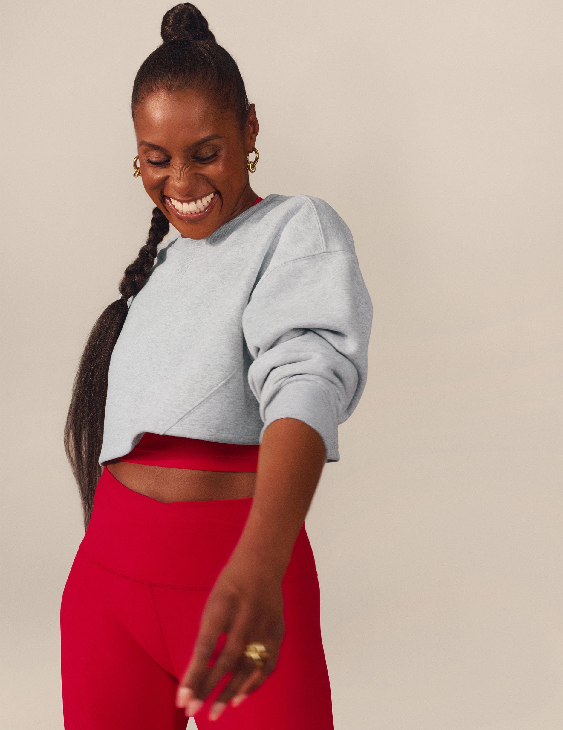 Issa Rae wearing a gray cropped sweatshirt and red pants against a beige background.