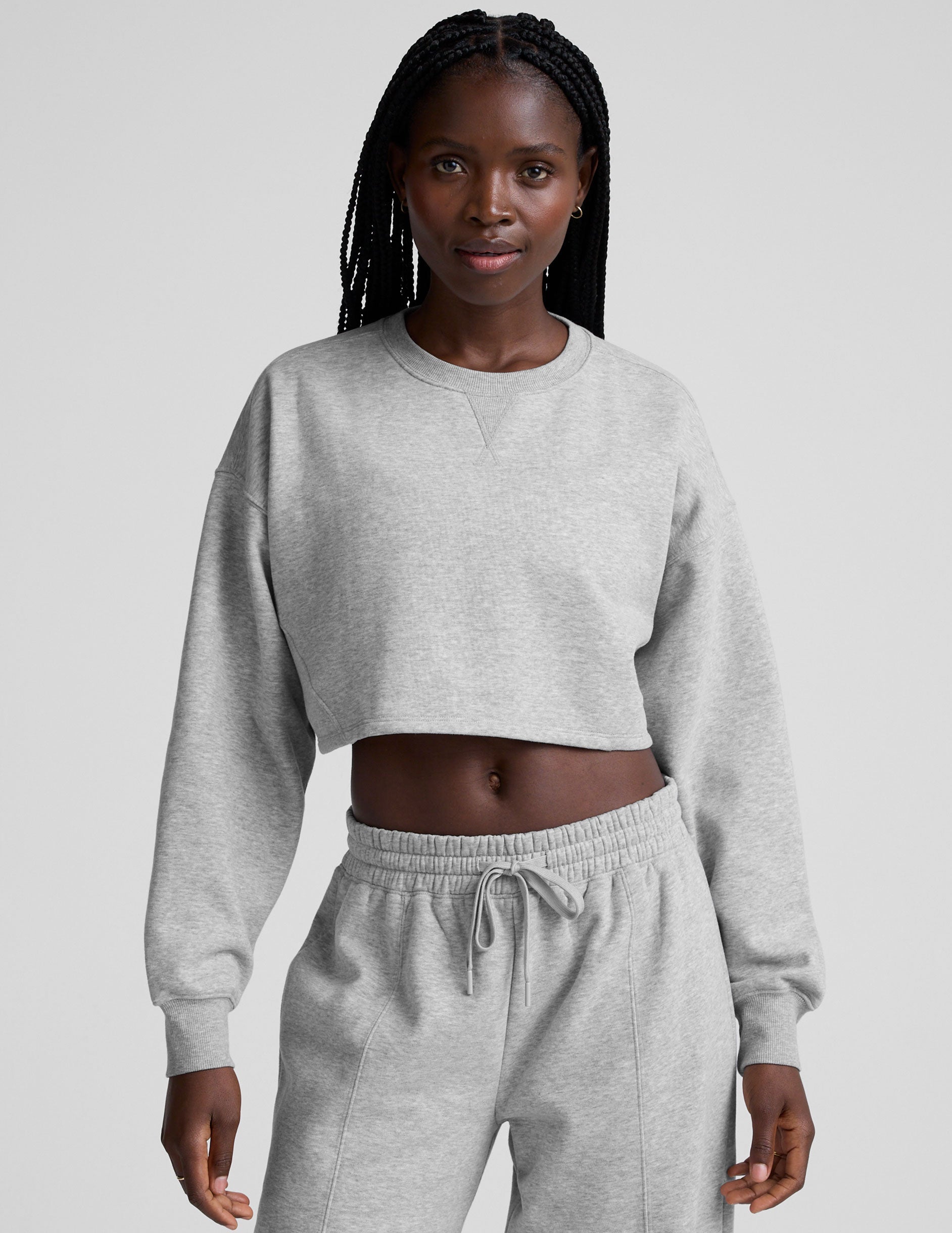 woman wearing a gray cropped sweatshirt and matching barrel fleece pants on a plain background.