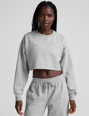 woman wearing a gray cropped sweatshirt and matching barrel fleece pants on a plain background.