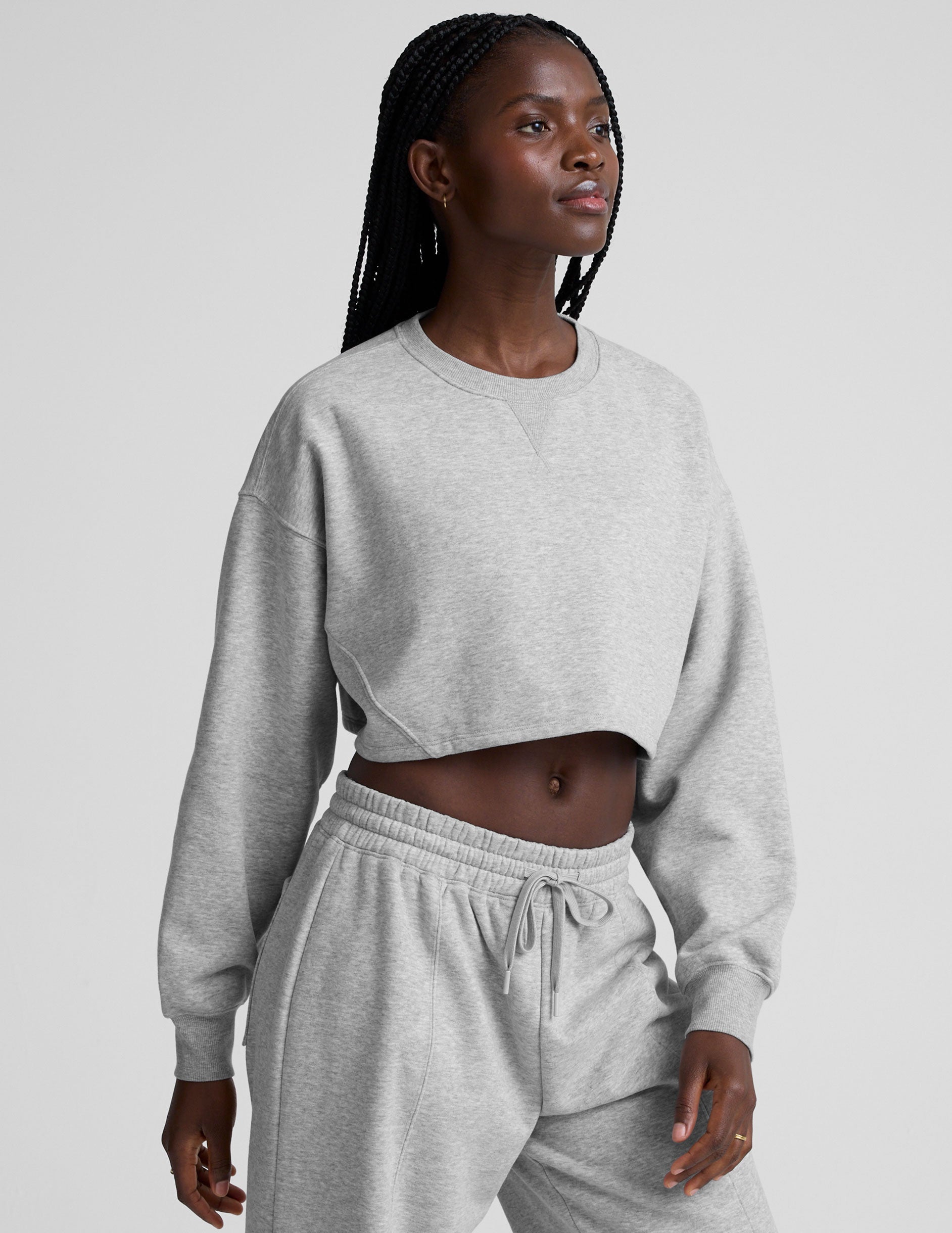 woman wearing a gray cropped sweatshirt and matching barrel fleece pants on a plain background.