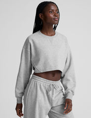 woman wearing a gray cropped sweatshirt and matching barrel fleece pants on a plain background.