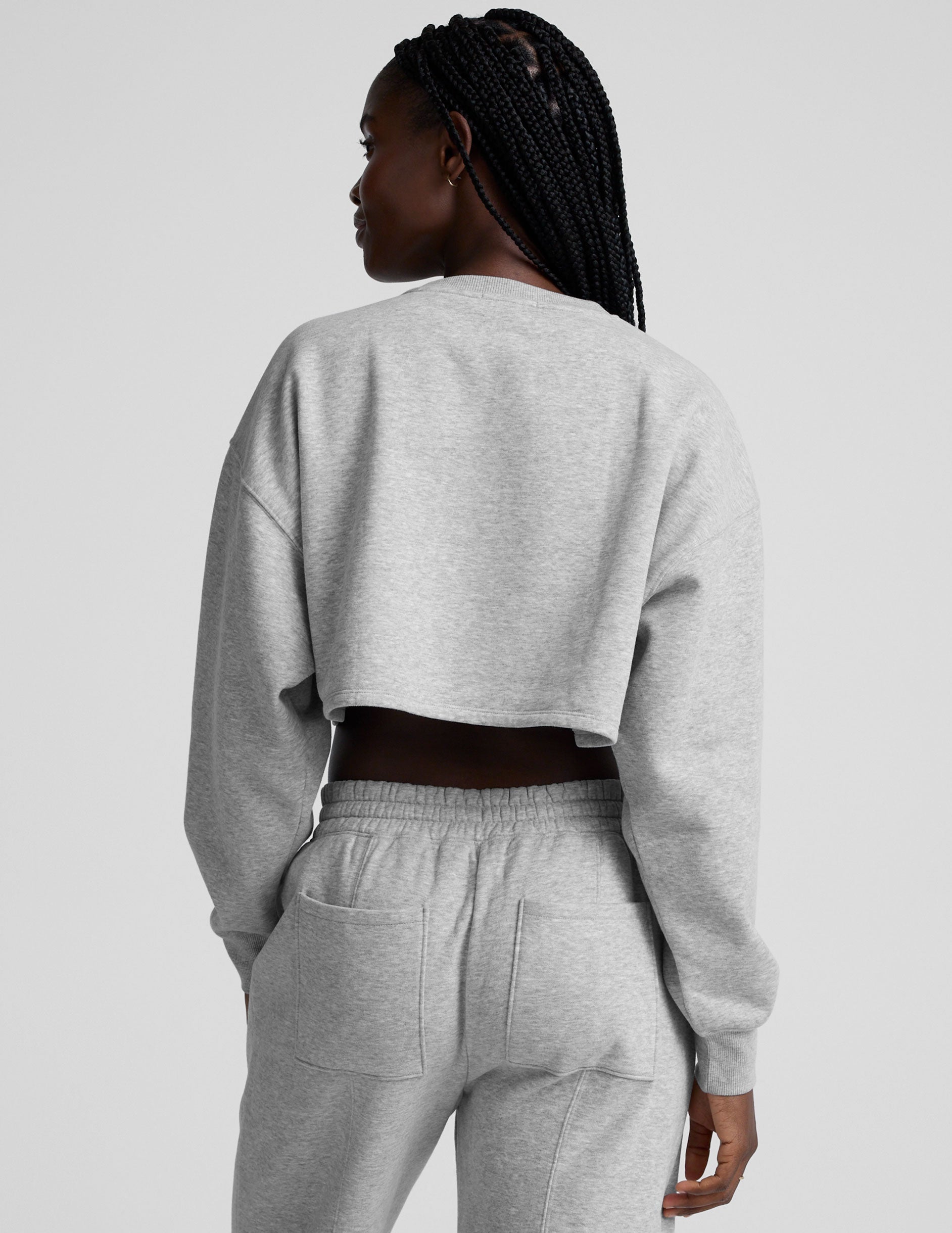 woman wearing a gray cropped sweatshirt and matching barrel fleece pants on a plain background.
