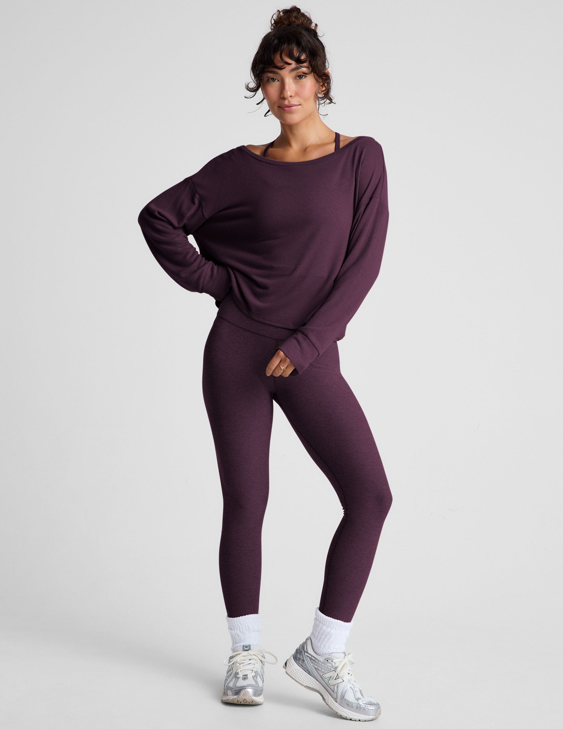 model wearing a dark purple long-sleeve boat neck sweater and leggings on a light gray background.