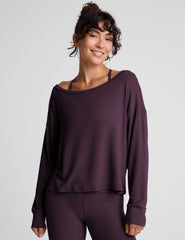 model wearing a dark purple long-sleeve boat neck sweater and leggings on a light gray background.