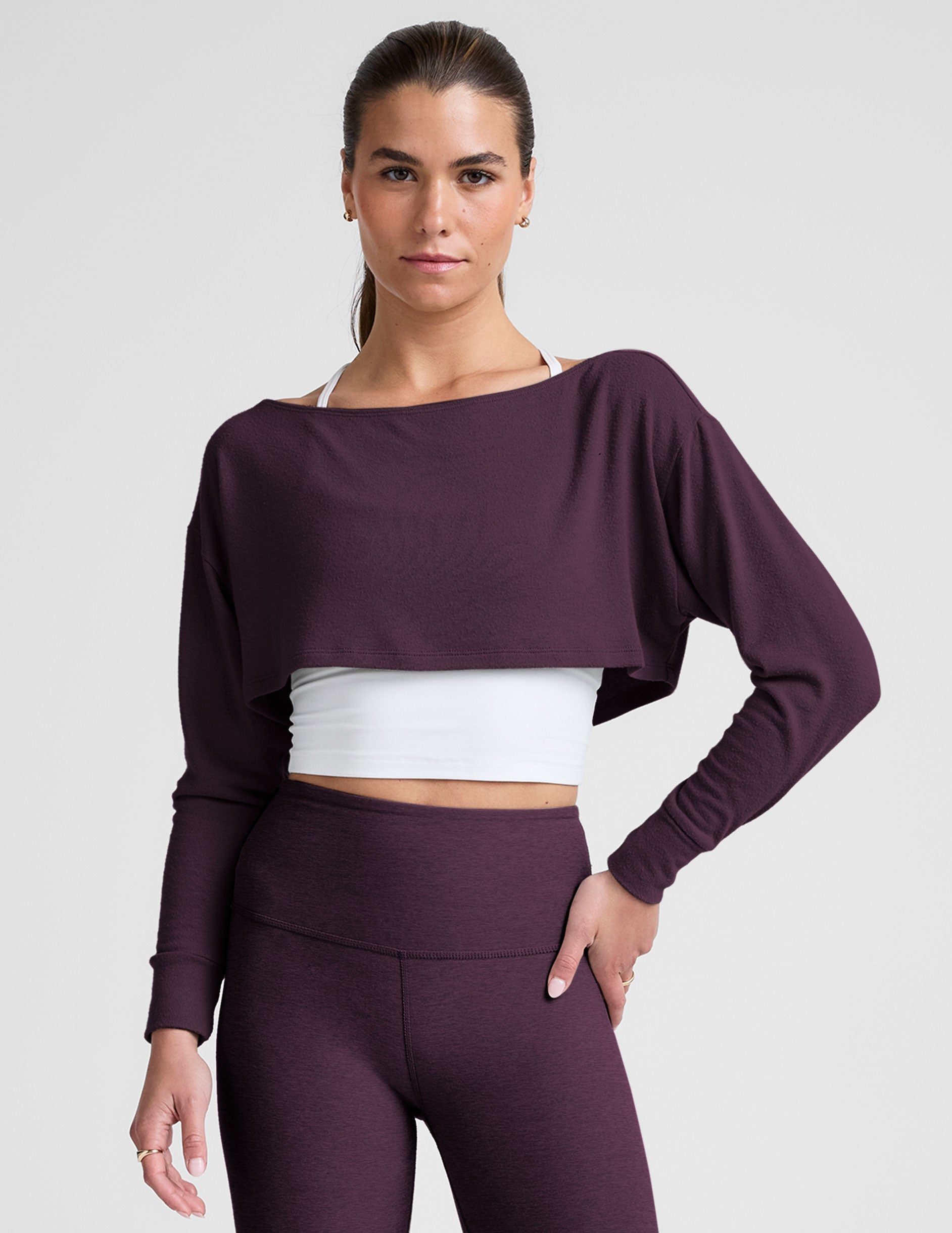 model wearing a white cropped tank and purple leggings with a purple shrug on a light background.