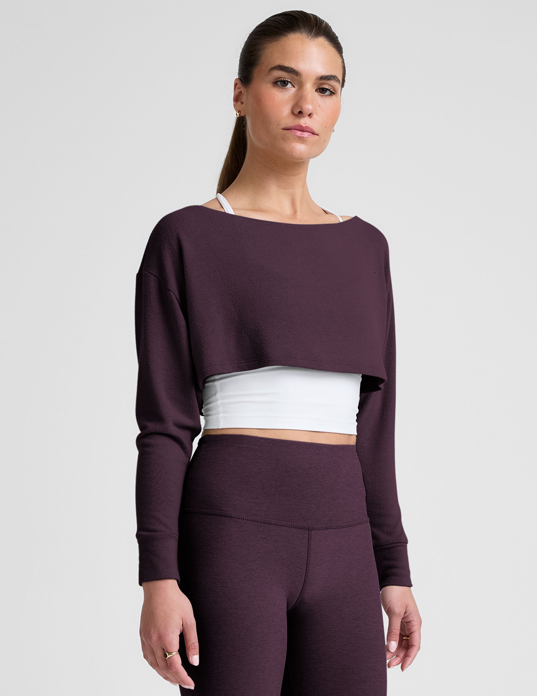 model wearing a white cropped tank and purple leggings with a purple shrug on a light background.