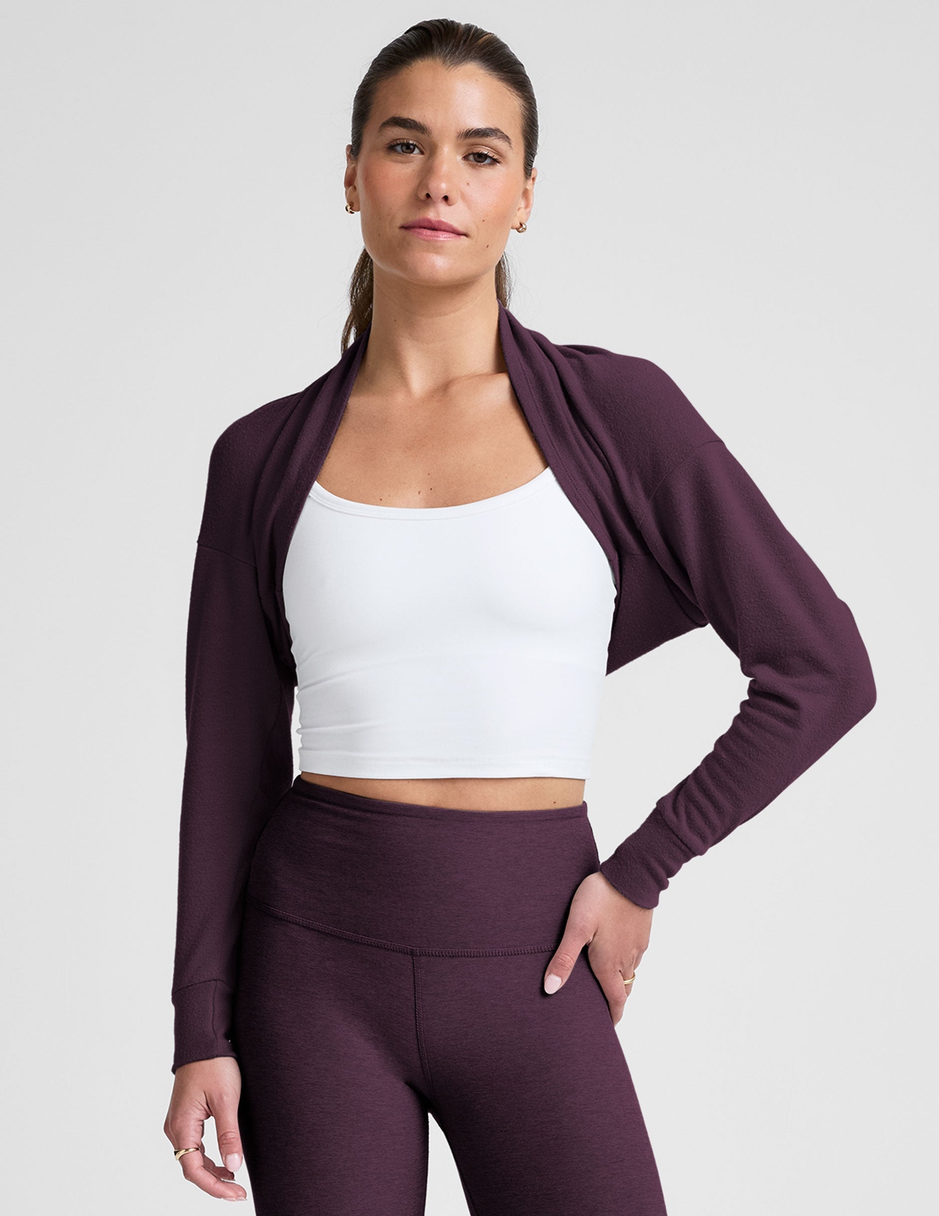model wearing a white cropped tank and purple leggings with a purple shrug on a light background.