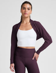 model wearing a white cropped tank and purple leggings with a purple shrug on a light background.