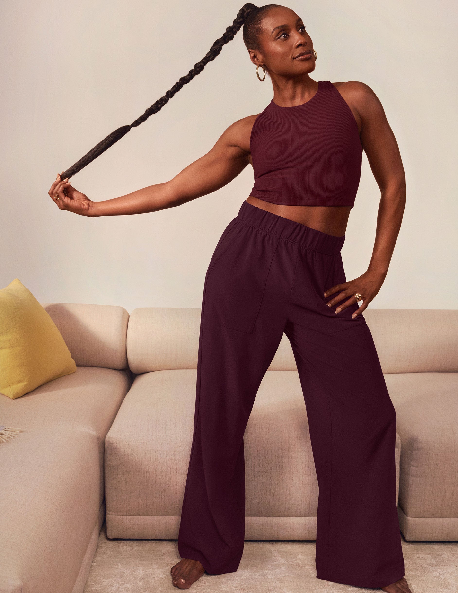 Issa Rae in burgundy top and wide-leg pants posing in a living room.