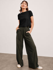 model wearing a black top and green wide-leg pants against a plain background.