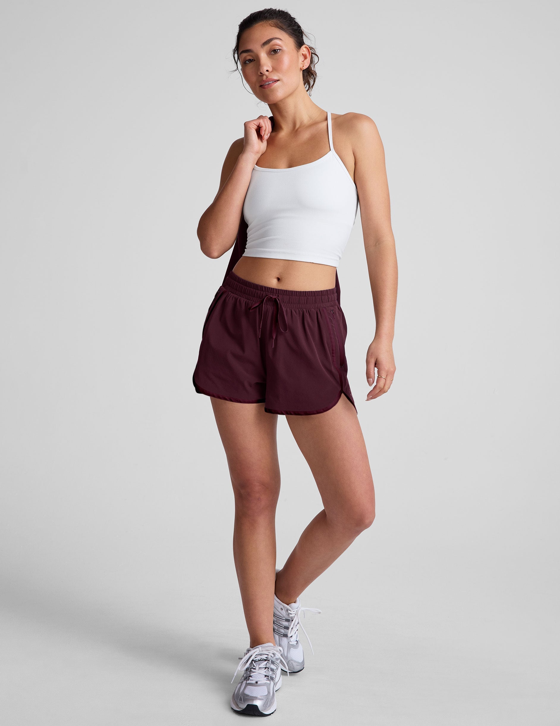 Woman wearing a white tank top and maroon shorts on a plain background